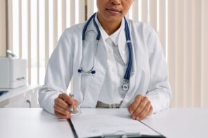 Médica do trabalho com estetoscópio preenchendo avaliação em prancheta