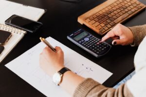 Mãos usando calculadora e anotando valores em papel sobre a mesa, ilustrando a apuração de desconto salarial