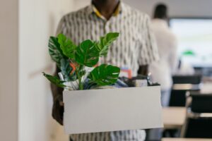 Homem carregando caixa com planta e objetos pessoais ao deixar o escritório