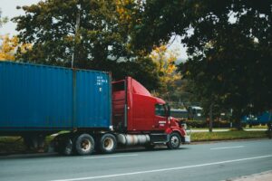 Caminhao vermelho transportando container azul em rodovia arborizada
