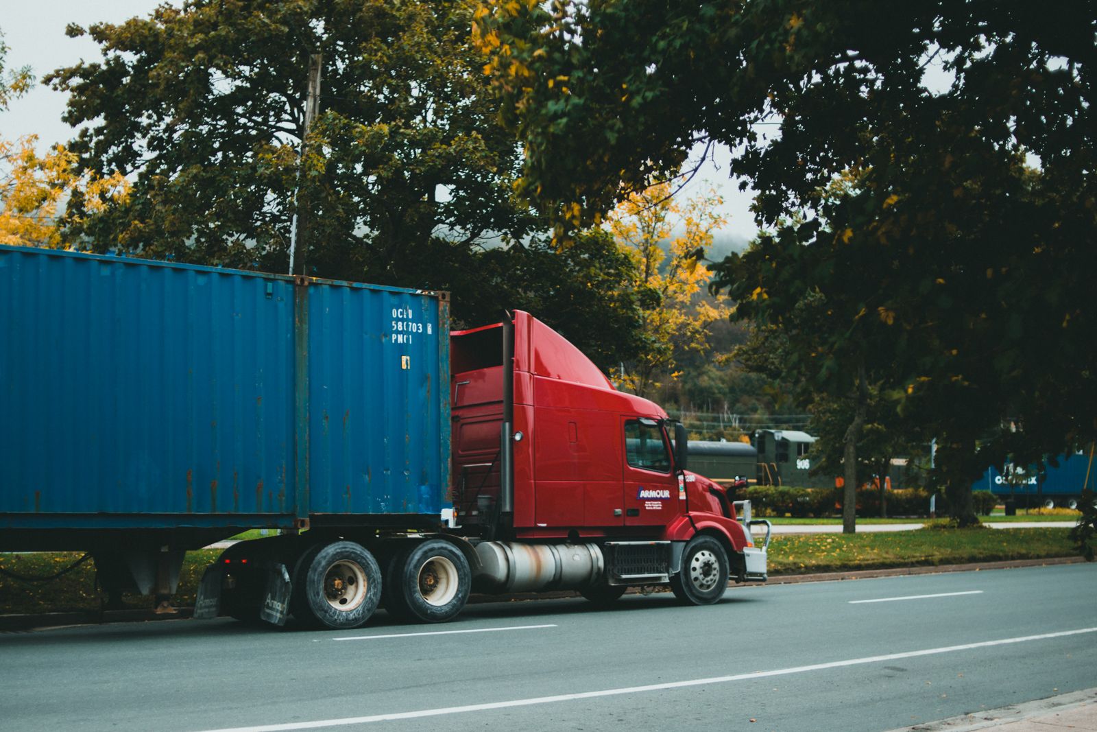 Caminhao vermelho transportando container azul em rodovia arborizada