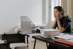 Mulher sentada a mesa de escritorio com as maos no rosto, olhando para papeis