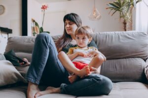 Mãe sentada no sofá segurando o filho pequeno no colo, em casa
