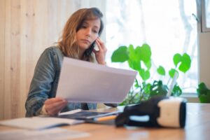 Mulher sentada a mesa falando ao telefone enquanto le um documento