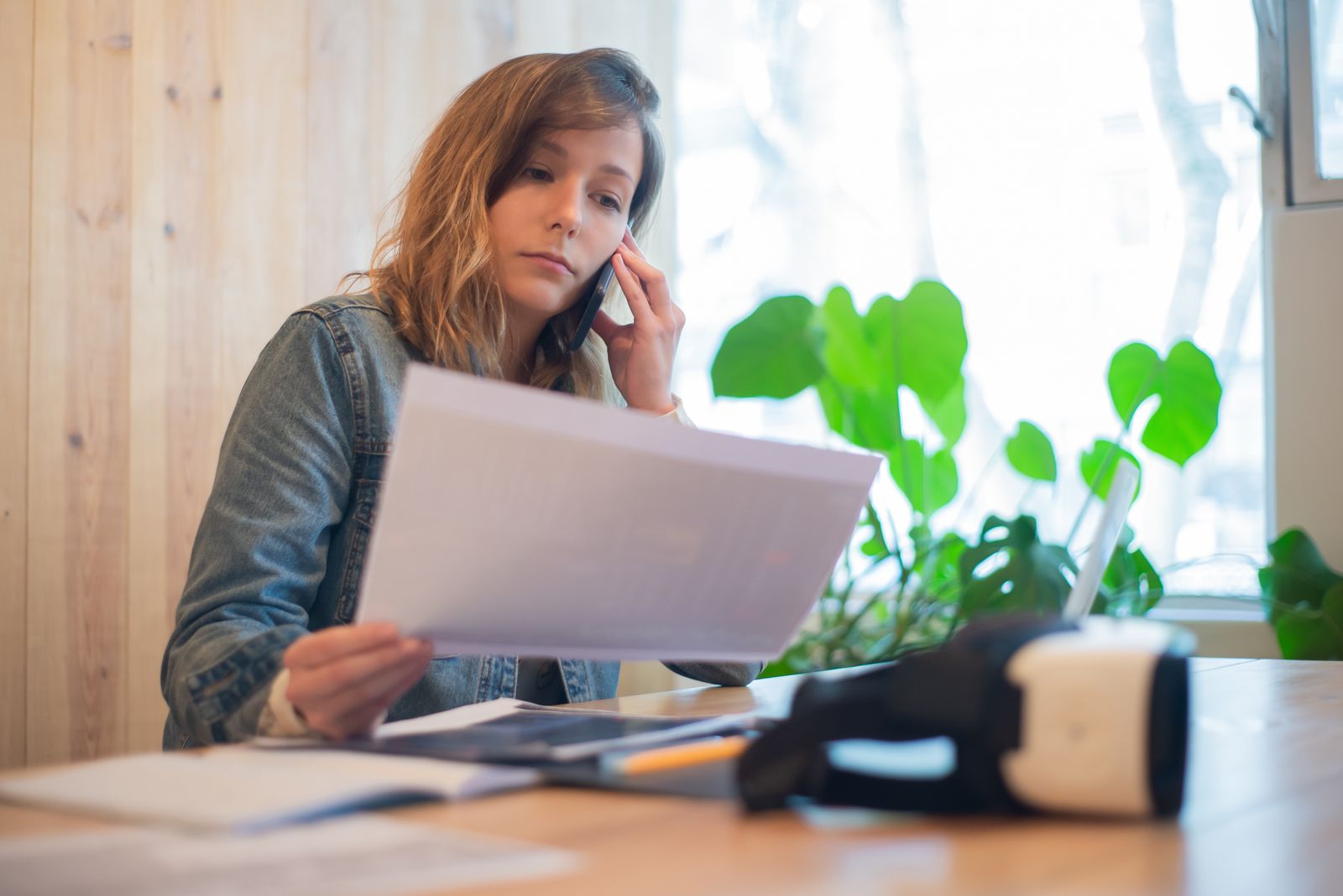 Mulher sentada a mesa falando ao telefone enquanto le um documento