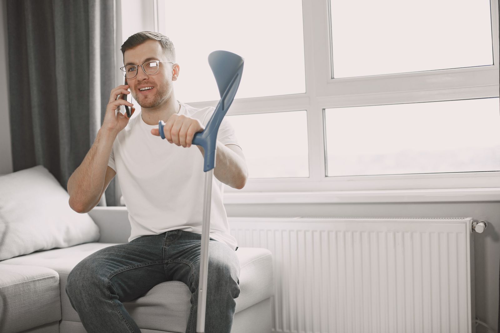 Homem com muleta sentado no sofá falando ao telefone