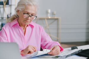 Mulher idosa de oculos conferindo documentos e comprovantes sobre a mesa em casa.
