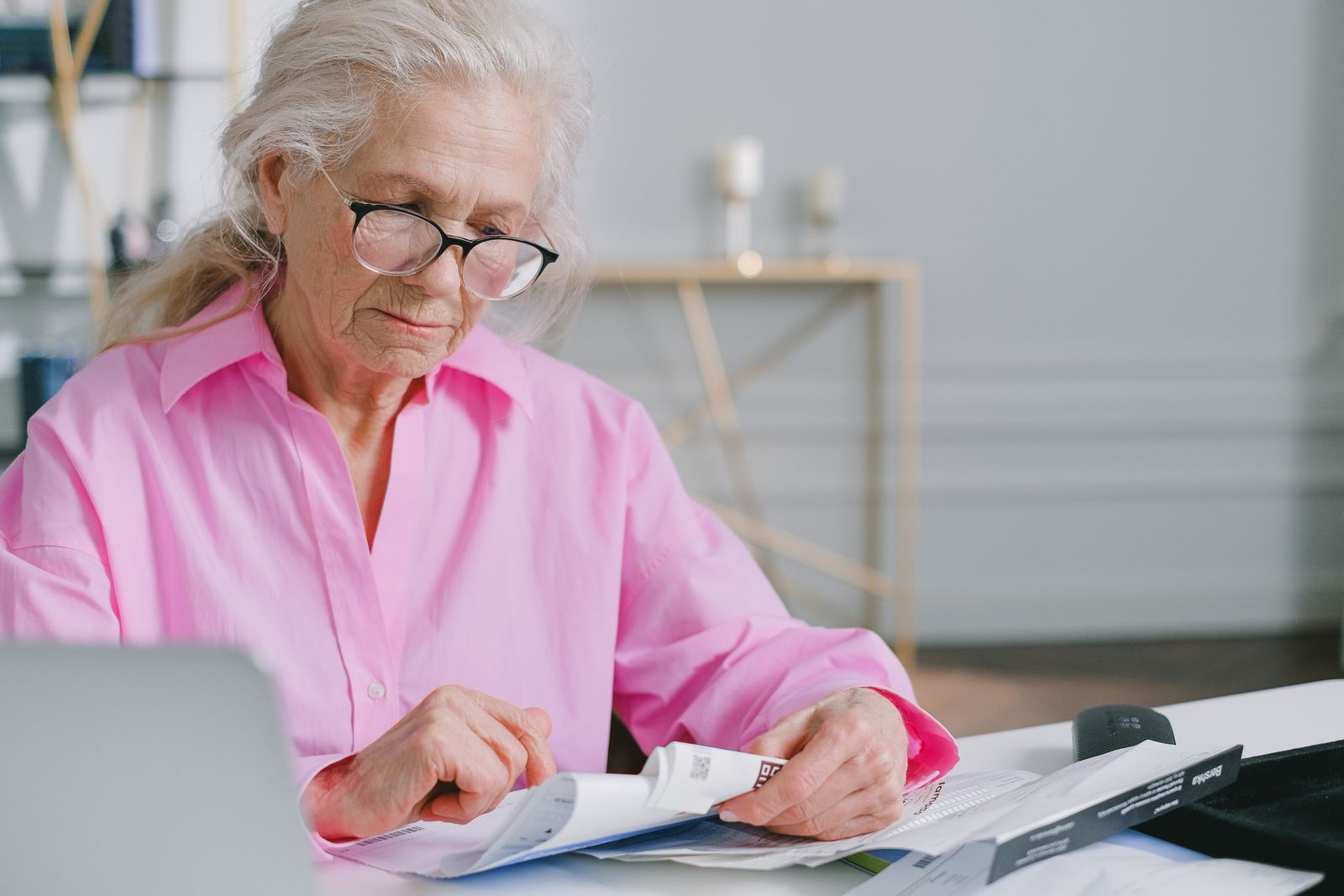 Mulher idosa de oculos conferindo documentos e comprovantes sobre a mesa em casa.
