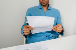 Pessoa sentada a mesa segurando um documento e uma caneta marcadora.