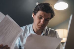 Homem lendo documentos impressos com expressão séria em ambiente interno