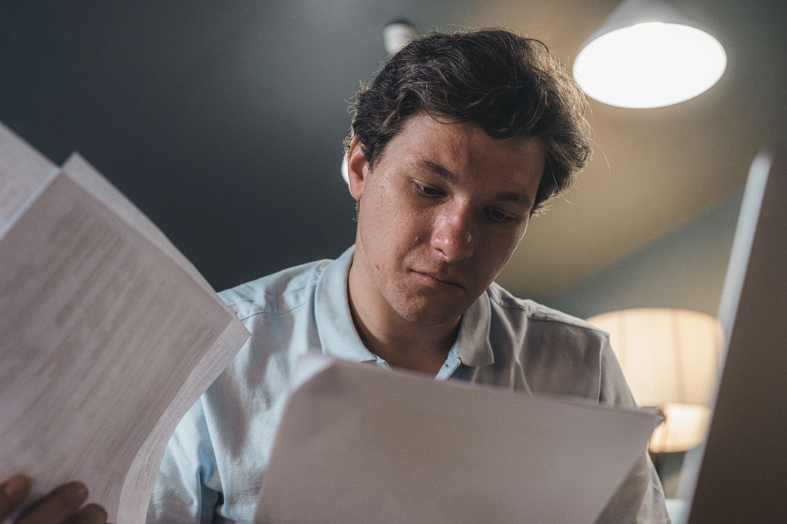 Homem lendo documentos impressos com expressão séria em ambiente interno