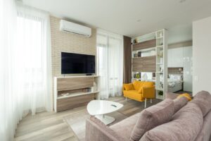 Sala de estar de apartamento moderno integrada a um quarto, com sofa, televisao e estante