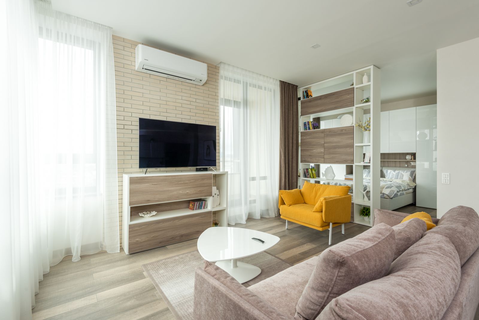 Sala de estar de apartamento moderno integrada a um quarto, com sofa, televisao e estante