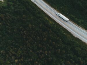 Vista aérea de uma carreta de carga trafegando em rodovia cercada por floresta