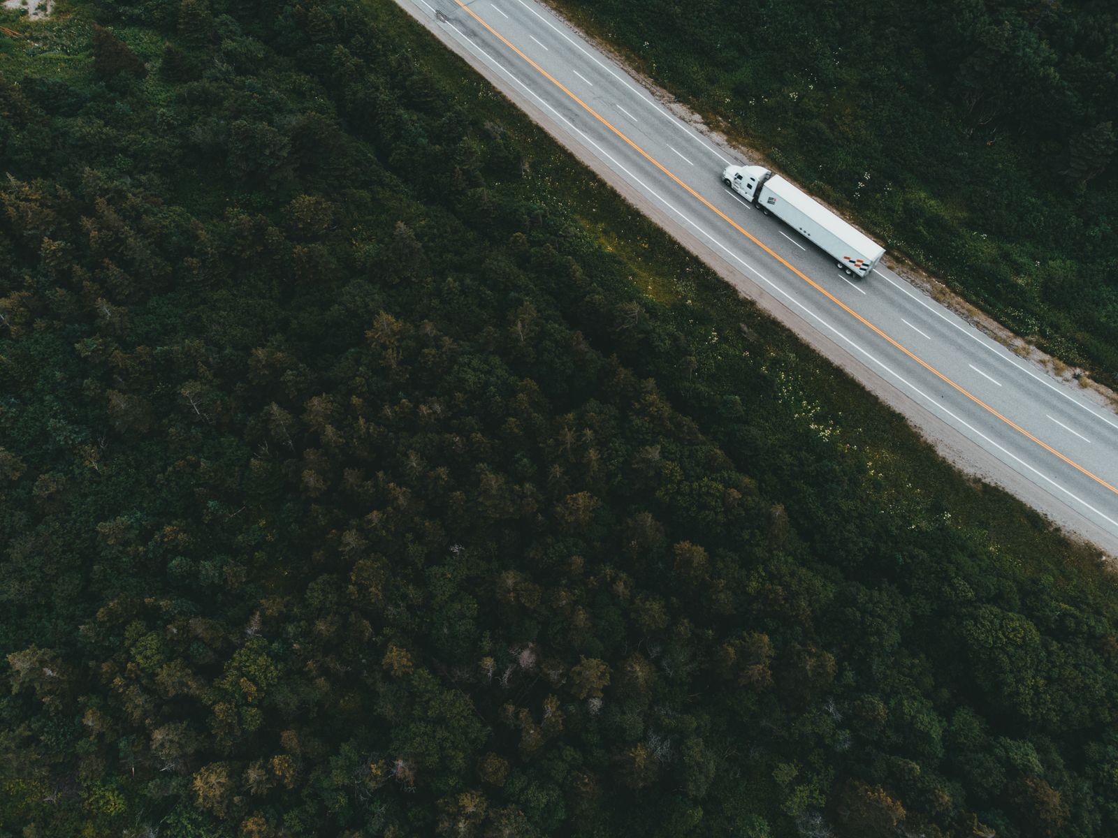 Vista aérea de uma carreta de carga trafegando em rodovia cercada por floresta