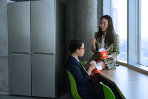 Duas colegas de trabalho almocando junto a janela de um escritorio no intervalo