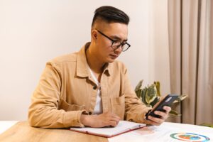 Homem à mesa de trabalho olhando a tela do celular com expressão preocupada